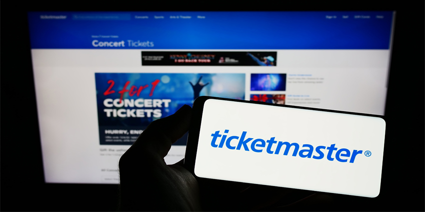 Person holding smartphone with logo of US company Ticketmaster Entertainment Inc. on screen in front of website. Focus on phone display.